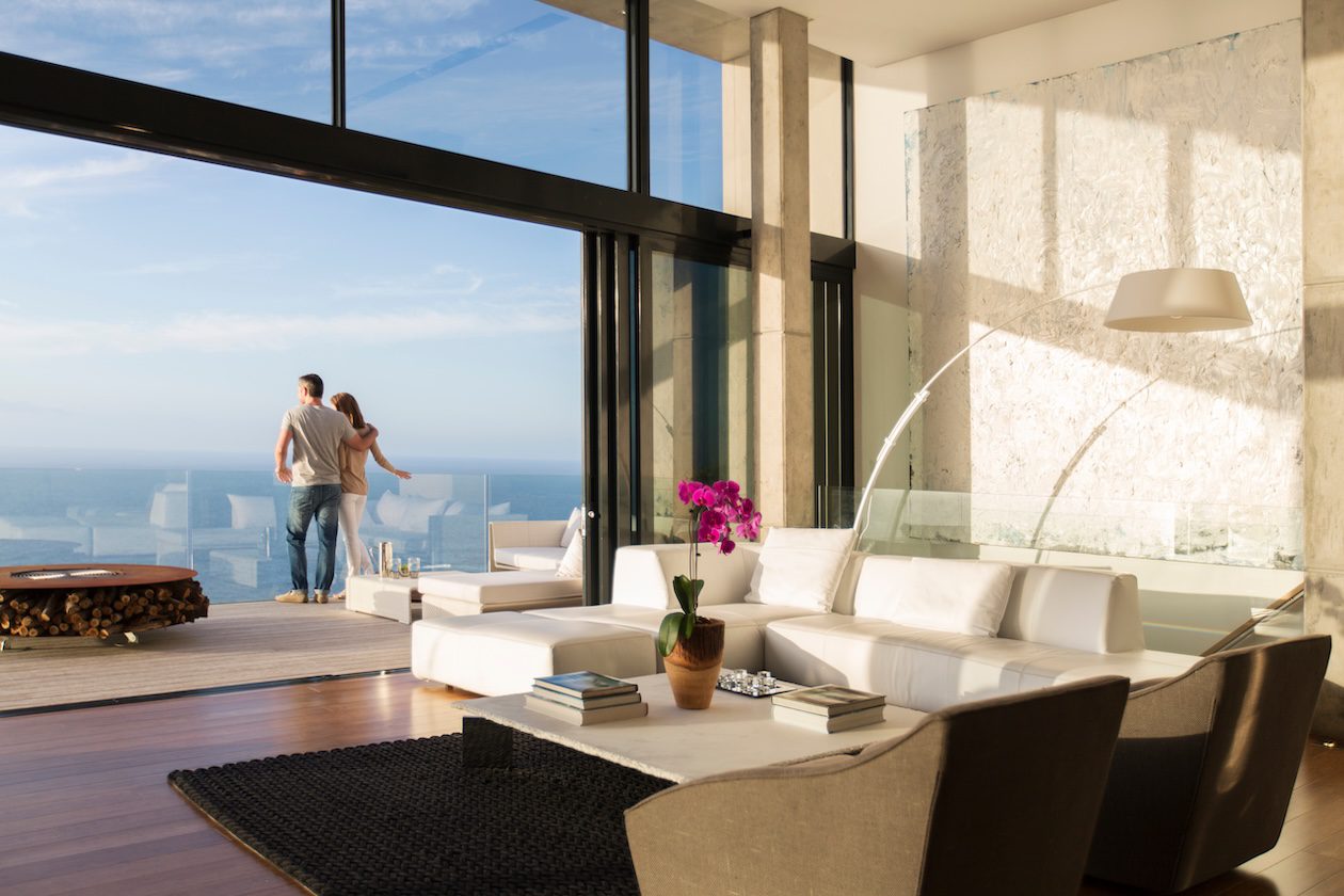 Couple standing on the balcony of a modern coastal home, overlooking an outdoor living space designed for relaxation and indoor-outdoor living in a San Diego–style setting.