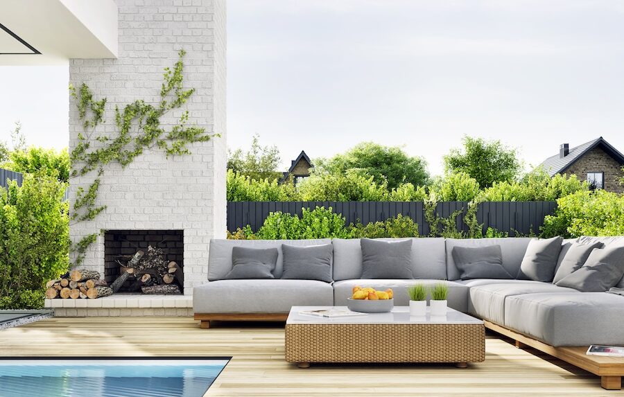 Outdoor patio with cushioned lounge furniture beside a swimming pool and modern outdoor fireplace, designed for sun exposure and coastal outdoor living.