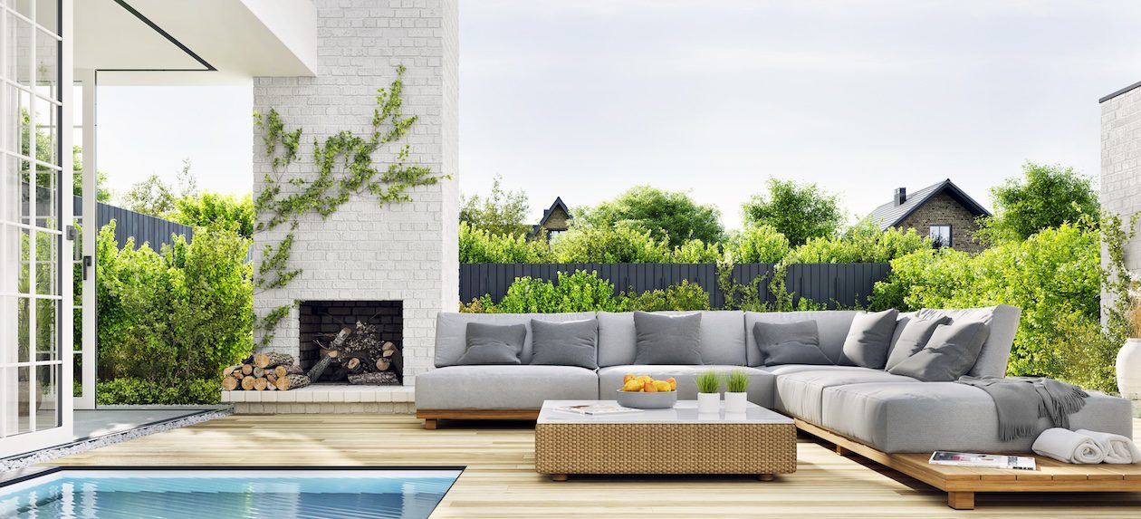 Outdoor patio with cushioned lounge furniture beside a swimming pool and modern outdoor fireplace, designed for sun exposure and coastal outdoor living.