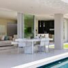 Modern coastal living room with slide-away glass doors opening to a patio and pool, creating a seamless indoor-outdoor living space with natural light and outdoor dining seating.