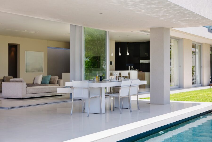 Modern coastal living room with slide-away glass doors opening to a patio and pool, creating a seamless indoor-outdoor living space with natural light and outdoor dining seating.