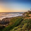 Sun setting over the northern end of Windansea Beach in San Diego, California, with golden light reflecting on ocean waves and rocky shoreline.