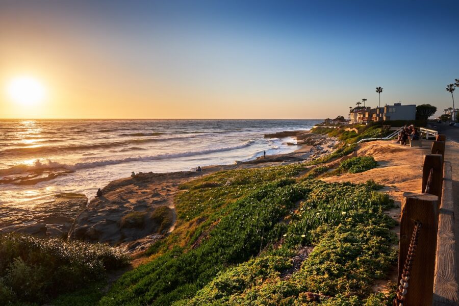 Sun setting over the northern end of Windansea Beach in San Diego, California, with golden light reflecting on ocean waves and rocky shoreline.