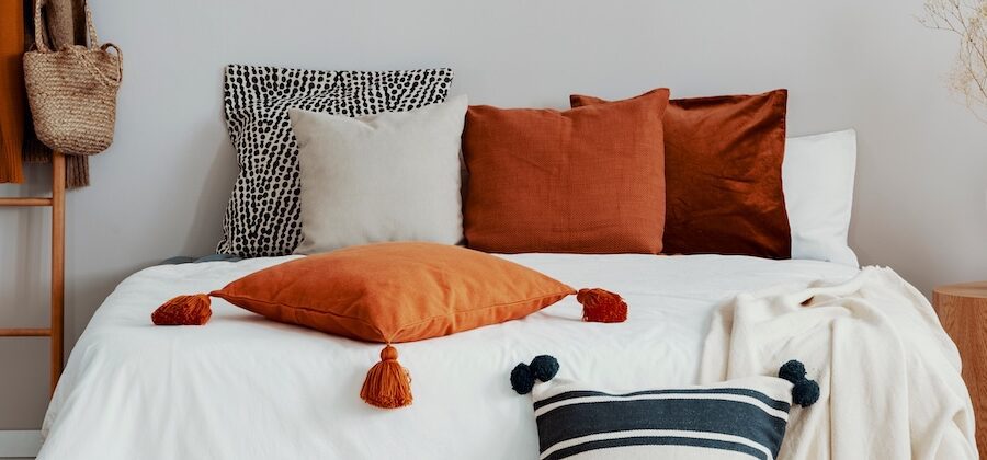Layered queen bed with Euro pillows, rust-colored decorative pillows, and a lumbar pillow styled on white bedding for a balanced, modern look
