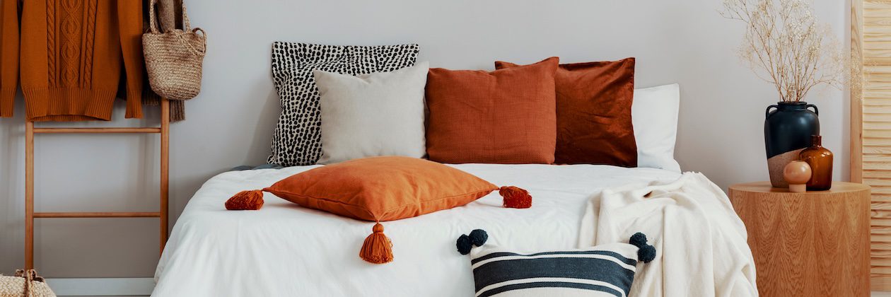 Layered queen bed with Euro pillows, rust-colored decorative pillows, and a lumbar pillow styled on white bedding for a balanced, modern look