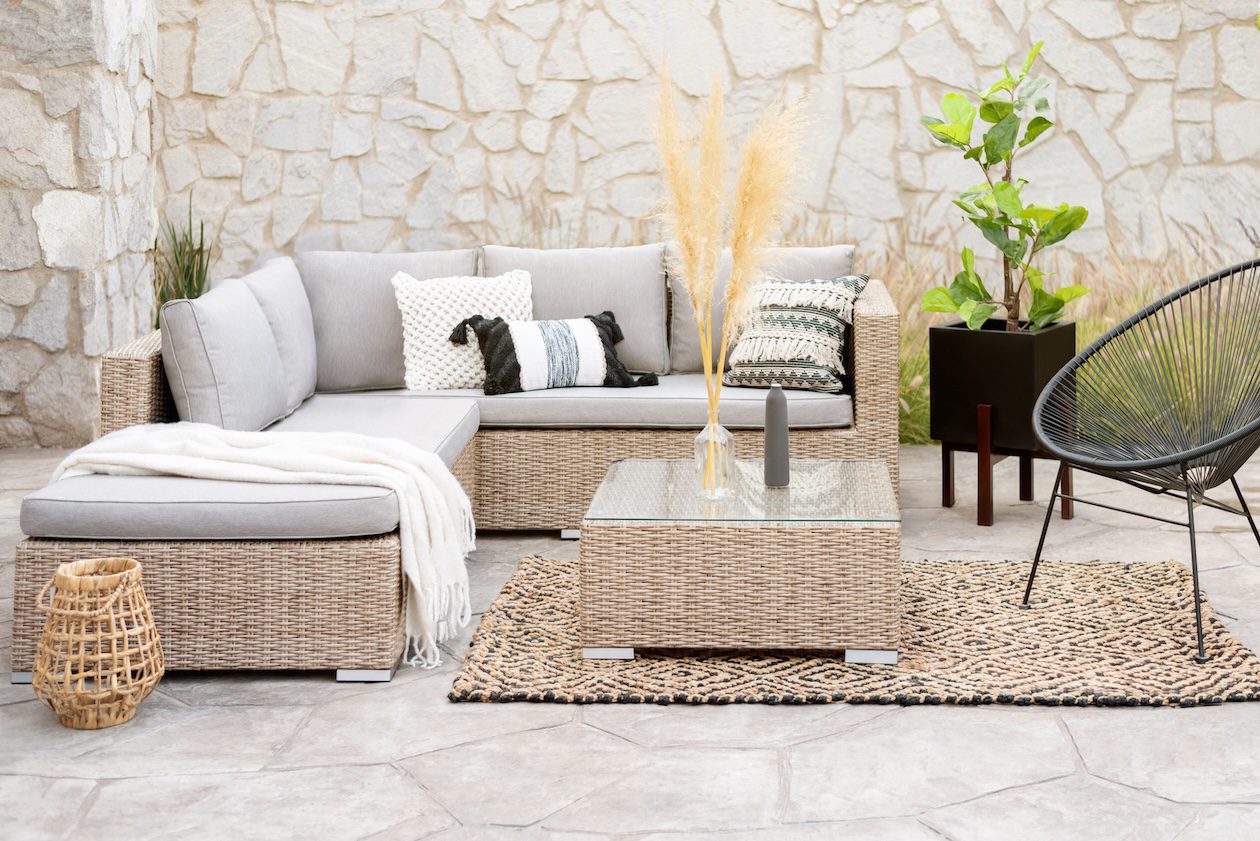 Outdoor rattan sectional sofa with neutral decorative pillows, wicker chairs, and a coffee table styled on a patterned rug in a modern patio living space