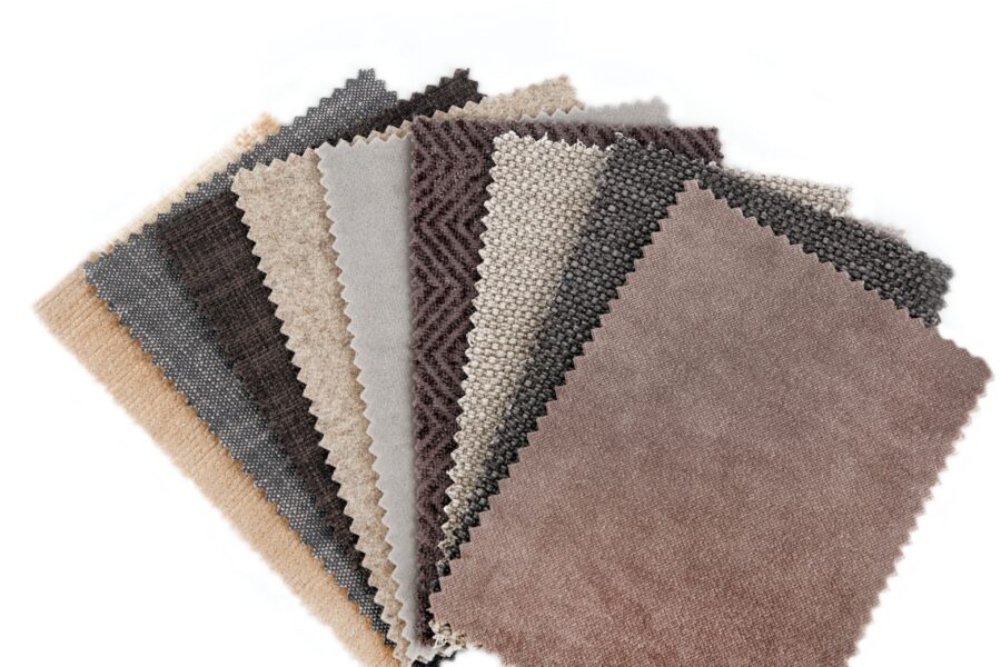 Collection of neutral-toned upholstery fabric swatches displaying various textures, weaves, and performance fabric finishes in shades of beige, gray, taupe, and brown.